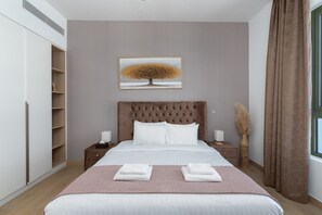 A modern bedroom with a large bed, a headboard, bedside tables, a wardrobe, and a window with curtains.