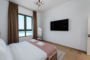 Une chambre d’hôtel avec un lit, un téléviseur fixé au mur, une fenêtre avec des rideaux et une vue sur la mer.