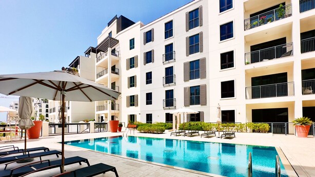 Un hotel moderno con piscina, mobiliario exterior y balcones.