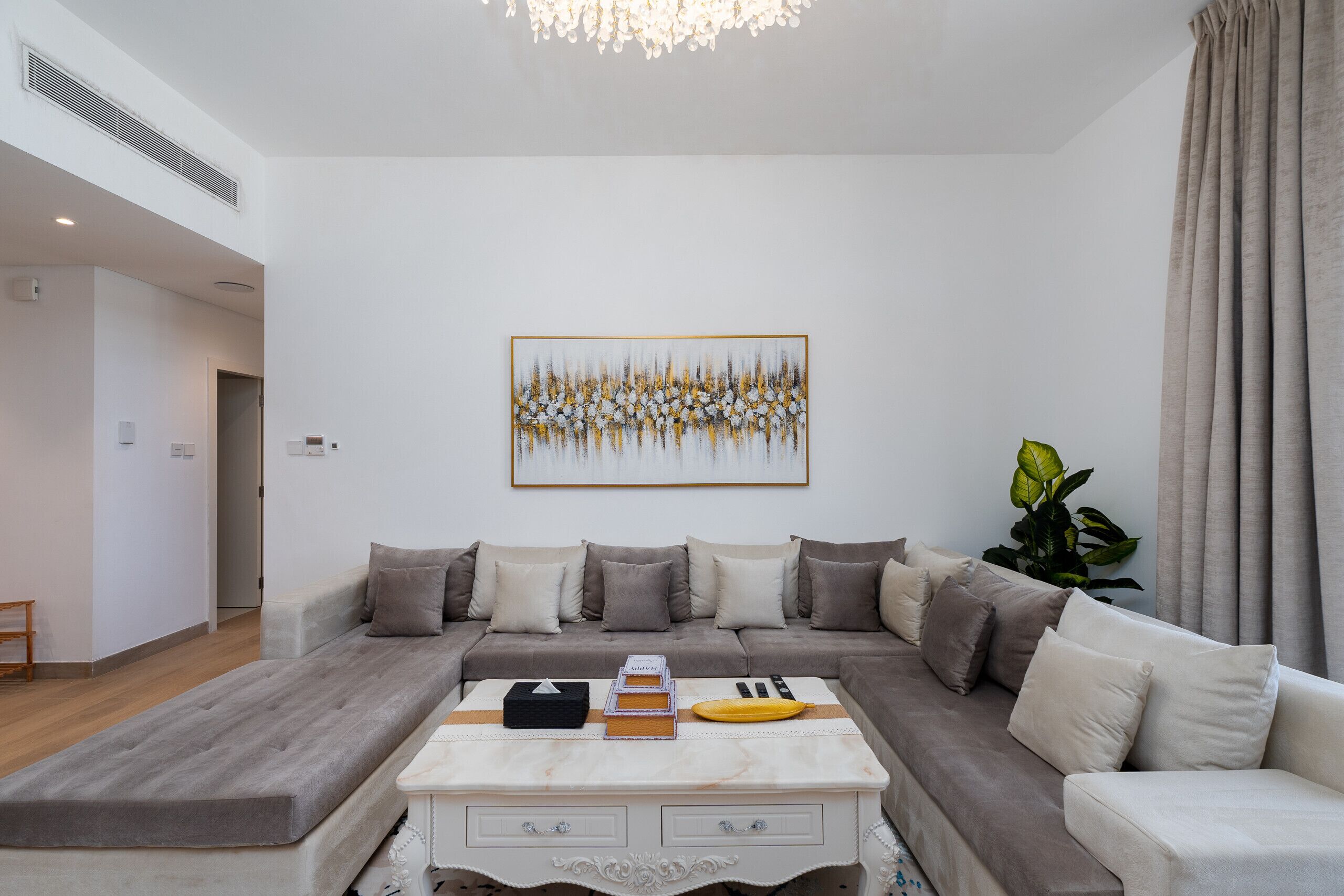 Ein modernes Wohnzimmer mit einer Eckcouch, einem Couchtisch mit Büchern und einer Banane, sowie einem großen abstrakten Gemälde an der Wand.
