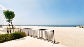 Una playa con cielo despejado, zona arenosa y valla metálica.
