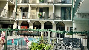 Un edificio de varios pisos con balcones, algunos adornados con coronas, y un área amurallada con piscina.