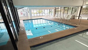 Piscina interior con carriles delimitados, una estación de socorristas y una zona de estar iluminada por el sol.