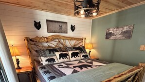 Un dormitorio rústico con estructura de cama de madera, colcha con diseños de osos y ventilador de techo.