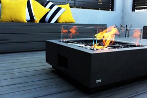A modern outdoor fire pit with a glass enclosure, placed on a wooden deck.