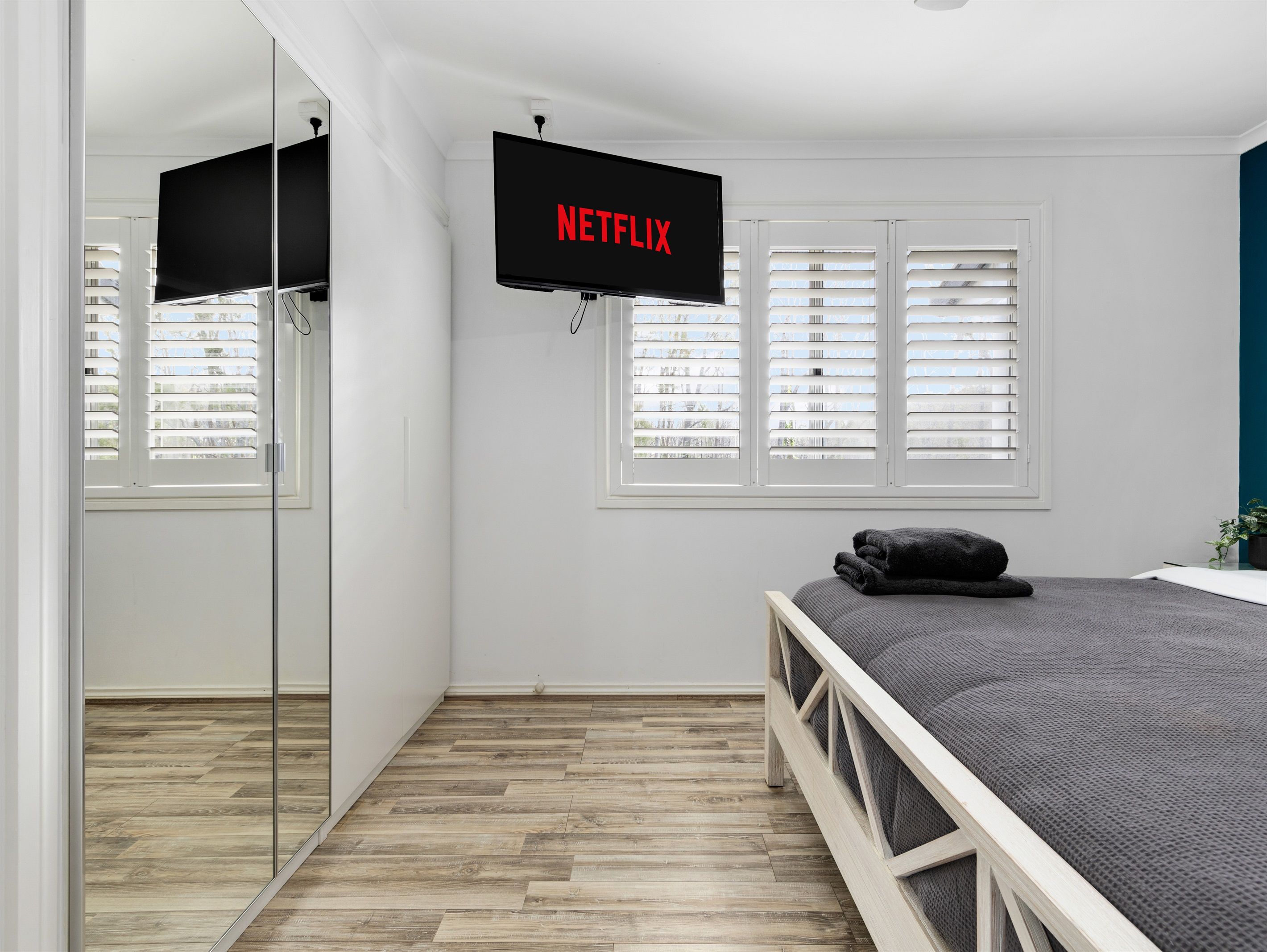 Een slaapkamer met een bed, een tv aan de muur en een raam met zonwering.