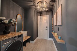 A hallway with a washing machine, a bench, a door, and a shelf with candles. - Magnolia Studio-Guest Unit (Houston)