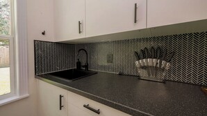 A kitchen with white cabinets, a black countertop, and a herringbone-patterned backsplash. - Magnolia Studio-Guest Unit (Houston)
