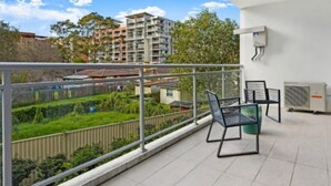 Un balcon donnant sur un quartier résidentiel, une table avec des chaises et un appareil de climatisation.