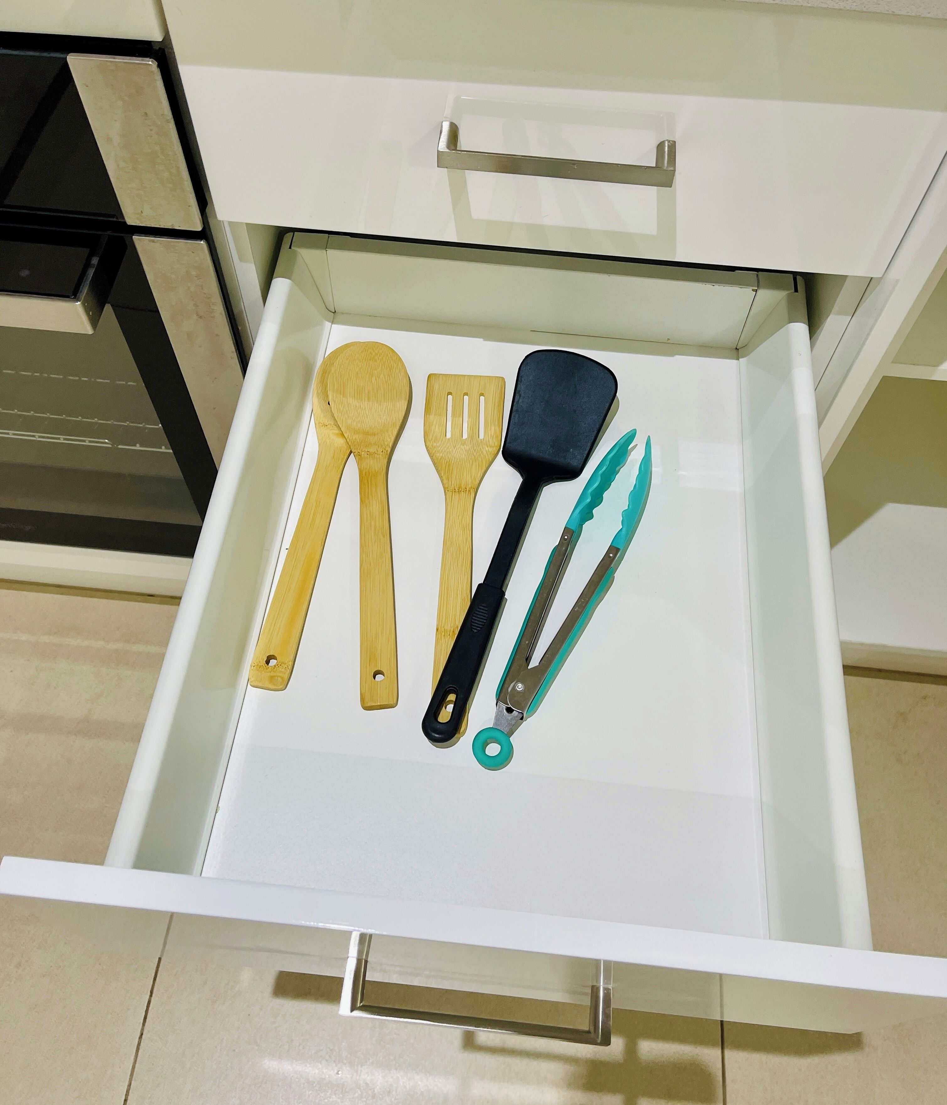Un tiroir contenant des ustensiles de cuisine, notamment des cuillères en bois, une spatule noire et une paire de ciseaux.