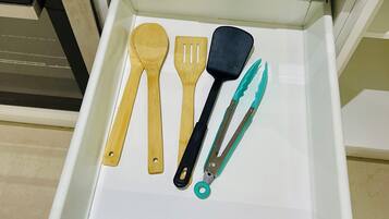 Un tiroir contenant des ustensiles de cuisine, notamment des cuillères en bois, une spatule noire et une paire de ciseaux.