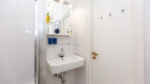 A bathroom with a white sink, a glass shelf with toiletries, and a door with a brass handle. - Jamé - Bright 2-room apartment with balcony, parking space and WLAN in Westerland. (Westerland)