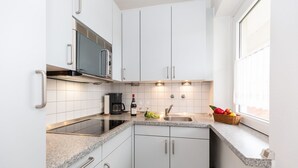 A modern kitchen with white cabinets, a black microwave, a coffee maker, and a fruit basket on the counter. - Jamé - Bright 2-room apartment with balcony, parking space and WLAN in Westerland. (Westerland)
