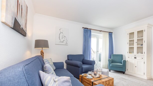 A living room with a blue sofa, a wooden coffee table, and a white cabinet. - Jamé - Bright 2-room apartment with balcony, parking space and WLAN in Westerland. (Westerland)
