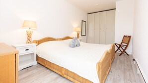 A bedroom with a bed, bedside tables, a chair, and a wardrobe. - Jamé - Bright 2-room apartment with balcony, parking space and WLAN in Westerland. (Westerland)