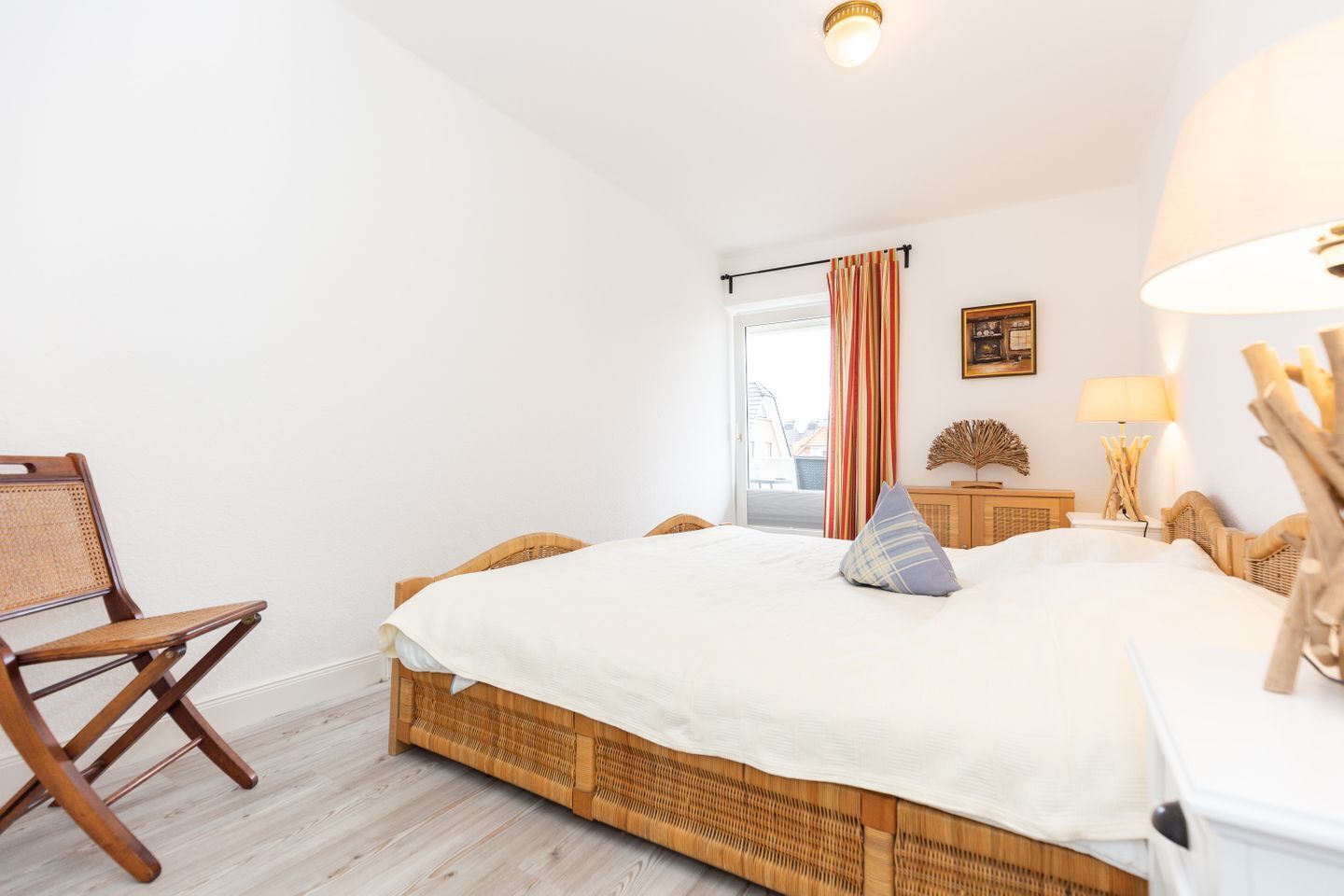 Quarto com cama grande, uma cadeira, mesa de cabeceira e janela com cortinas.