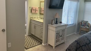 Une salle de bain équipée d’un lavabo, d’un miroir, d’un porte-serviettes et d’un téléviseur fixé au mur.