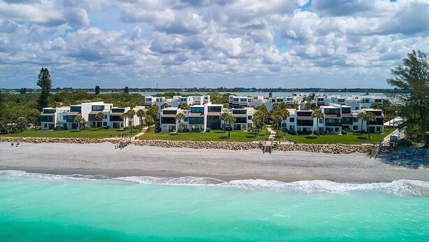 Un complexe hôtelier situé en bord de mer, composé de plusieurs bâtiments modernes, doté d’une plage de sable fin et bordé d’eaux turquoise et cristallines.
