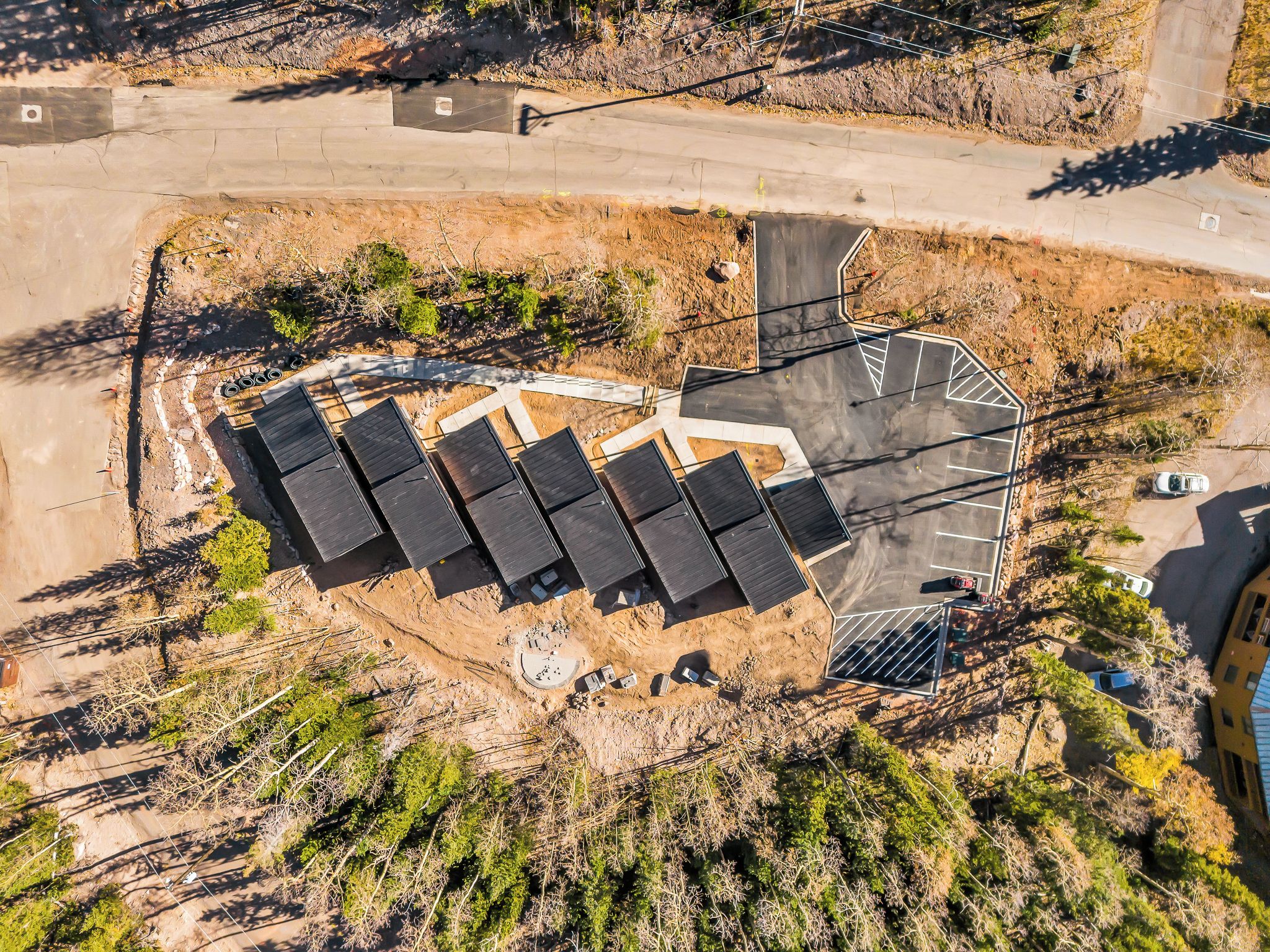 An aerial view of a parking area with multiple rows of solar panels, a paved walkway, and a small building structure.