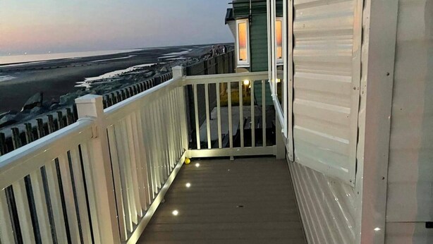 Een balkon met een houten vloer en witte leuningen, met uitzicht op een strand en de oceaan.