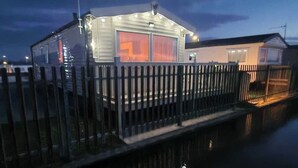 Een huis aan het water met een omheinde steiger, grote ramen en een zichtbare garage.
