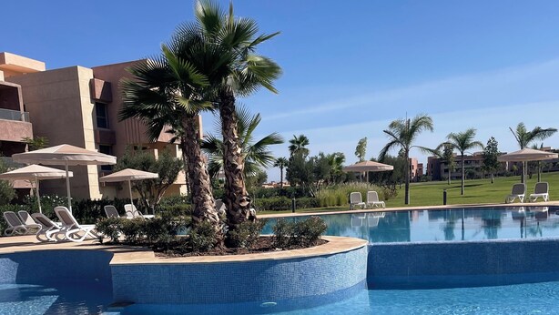 A swimming pool with clear blue water, surrounded by lounge chairs and palm trees. - Marrakech Prestigia Piscine Golf Saphir (Marrakech)