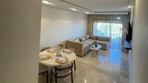 A spacious living area with a dining table set for four, a sofa, and a television mounted on the wall. - Marrakech Prestigia Piscine Golf Saphir (Marrakech)