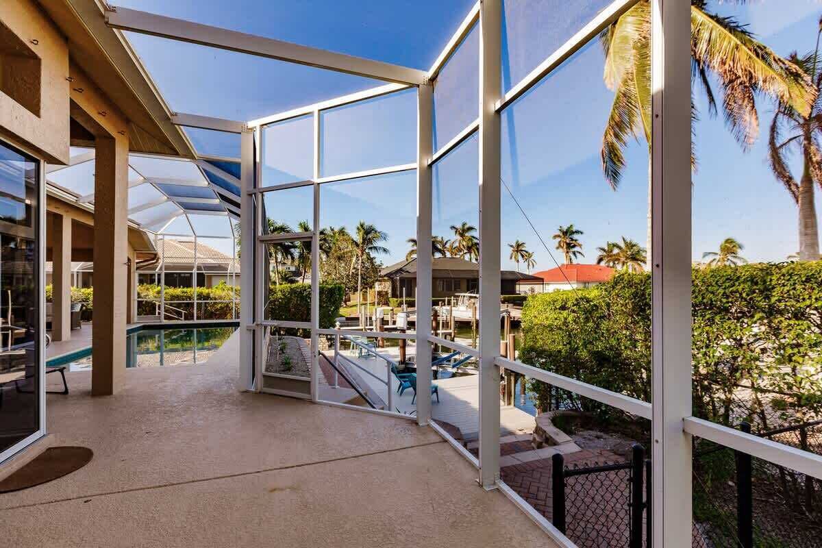 A covered outdoor area with glass walls, a pool, and palm trees.