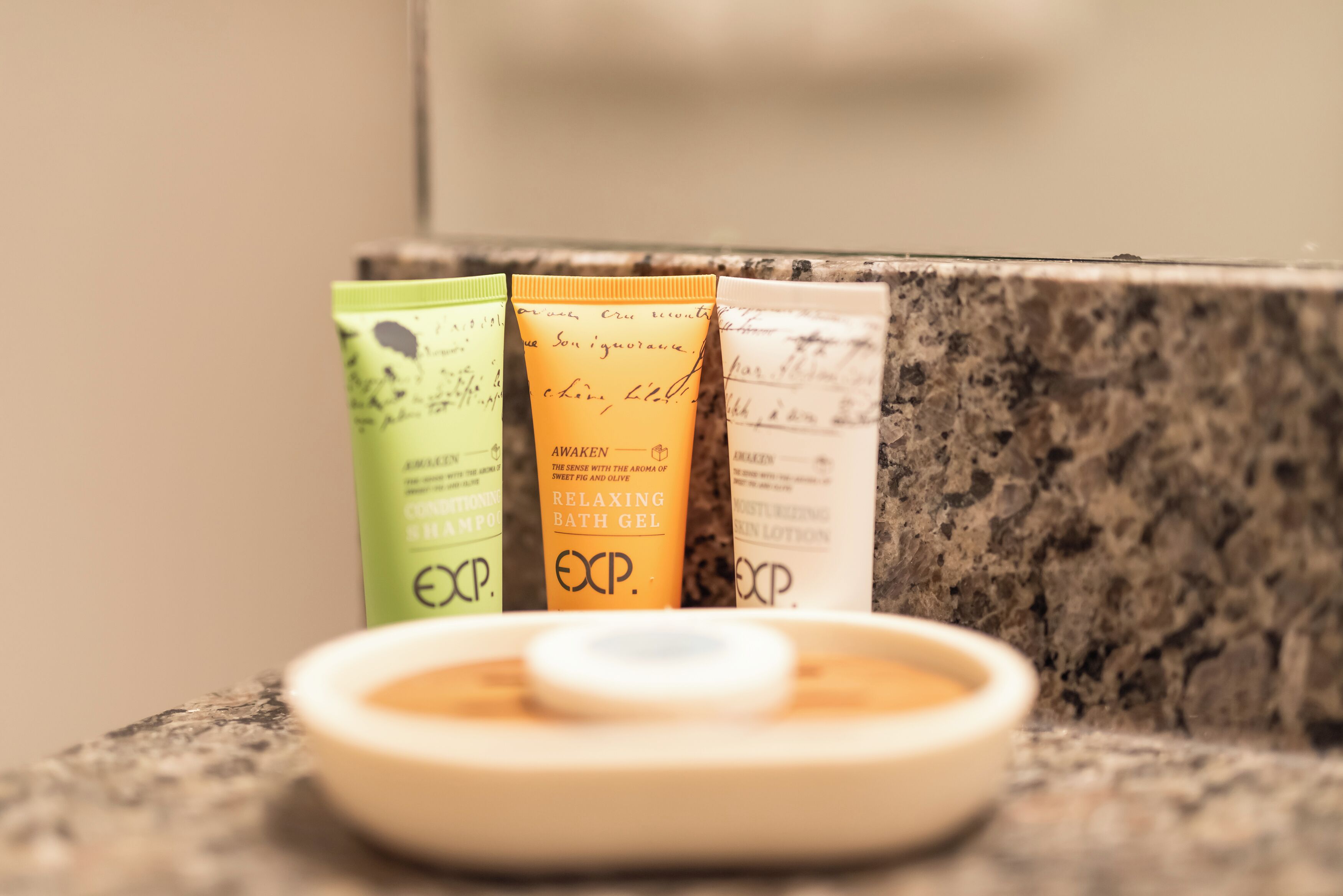 A bathroom counter with three toiletry items: a green lotion, an orange bath gel, and a white lotion.
