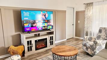 A living room with a flat-screen TV on a wooden stand, a fireplace, and floral-patterned sofas.
