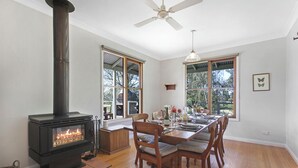 A dining area with a wood-burning stove, large windows, and a ceiling fan. - Country House Retreat (Nungurner)