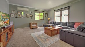 A living room with a large flat-screen TV, a leather sofa, a wicker chair, and a coffee table. - Country House Retreat (Nungurner)
