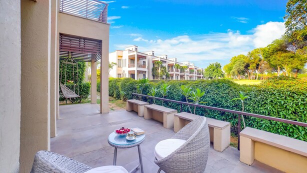 Ein Balkon mit Korbstühlen und einem kleinen Tisch, mit Blick auf eine Wohngegend mit ordentlich geschnittenen Hecken und mehrstöckigen Gebäuden.