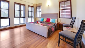 Ein geräumiges Schlafzimmer mit einem großen Bett, mehreren Fenstern, Holzboden und einer Essecke mit einem Stuhl.