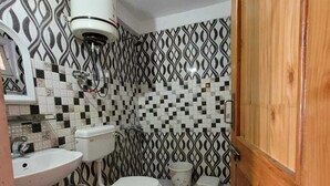 A bathroom with a patterned tile wall, a toilet, a sink, and a wooden door. - Hills Homestay and Devallya (Manali)