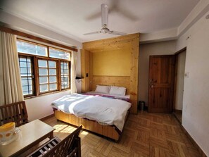 Une chambre à coucher avec une tête de lit en bois, un lit avec une literie blanche, une table en bois avec des chaises et une fenêtre avec des rideaux.