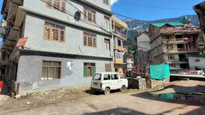 A multi-story building with a flat roof and a white van parked in front. - Hills Homestay and Devallya (Manali)