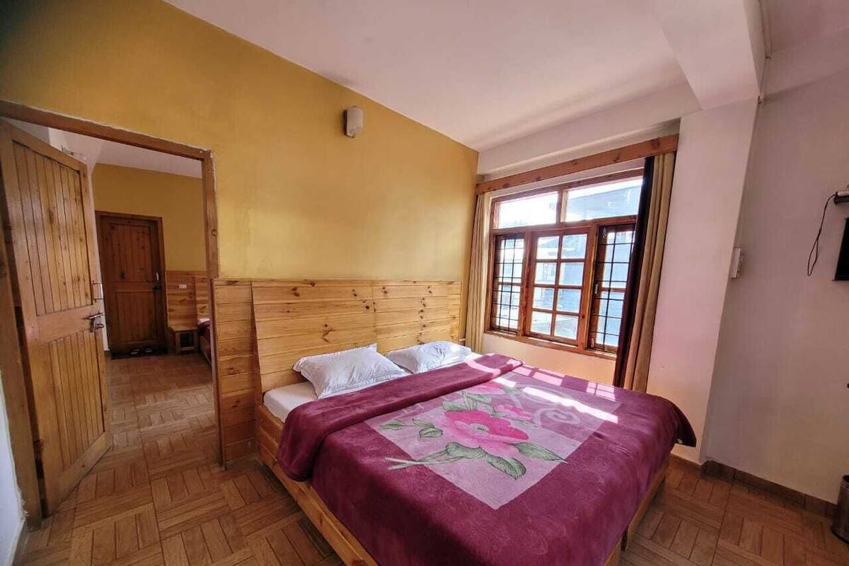 A bedroom with a wooden headboard, a large window with curtains, and a wooden floor.