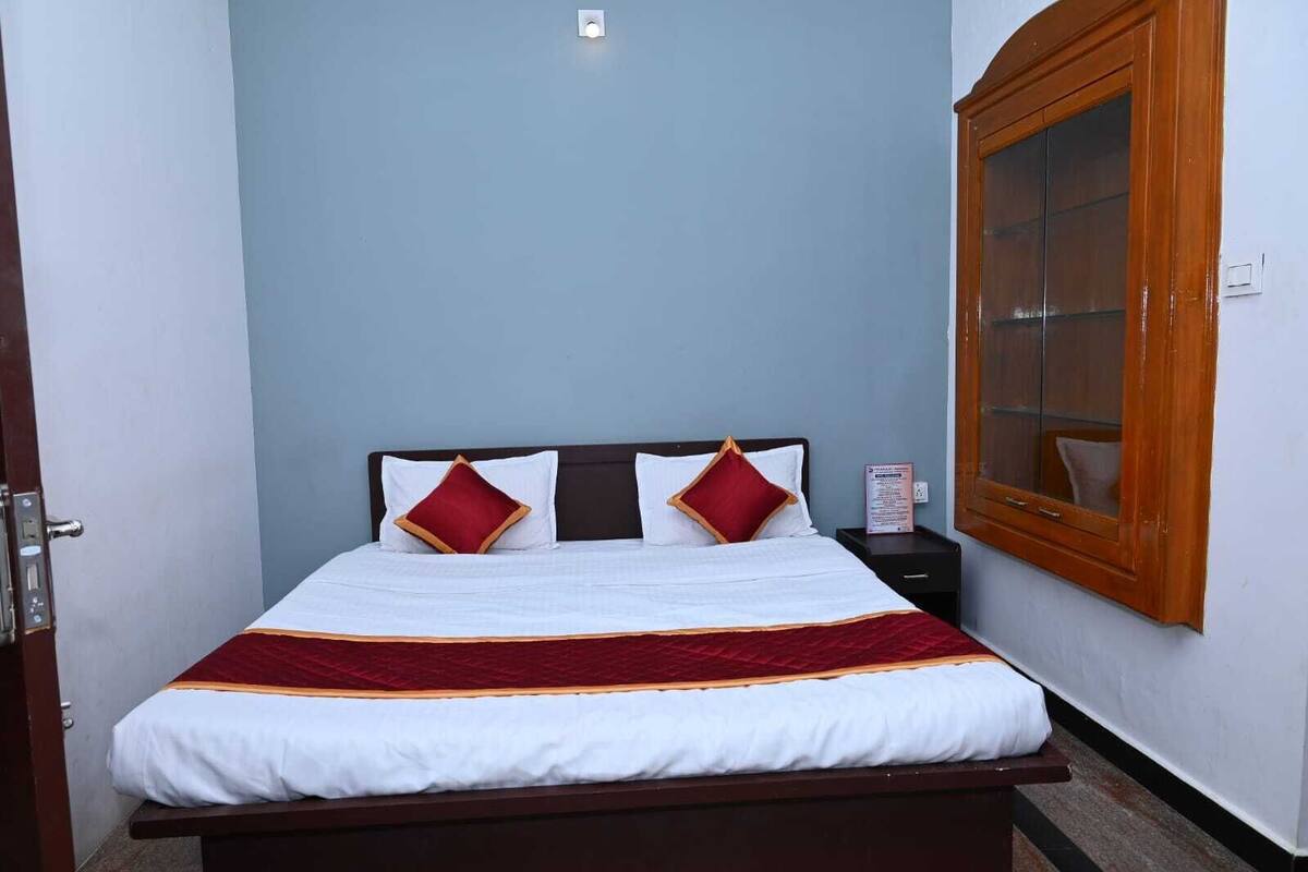 A neatly made bed with white bedding and red accents, a wooden headboard, and a window with a wooden frame.