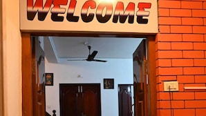 A hallway with a 'WELCOME' sign at the entrance, leading to a room with two doors and a ceiling fan. - Prakash Residence (Puducherry)