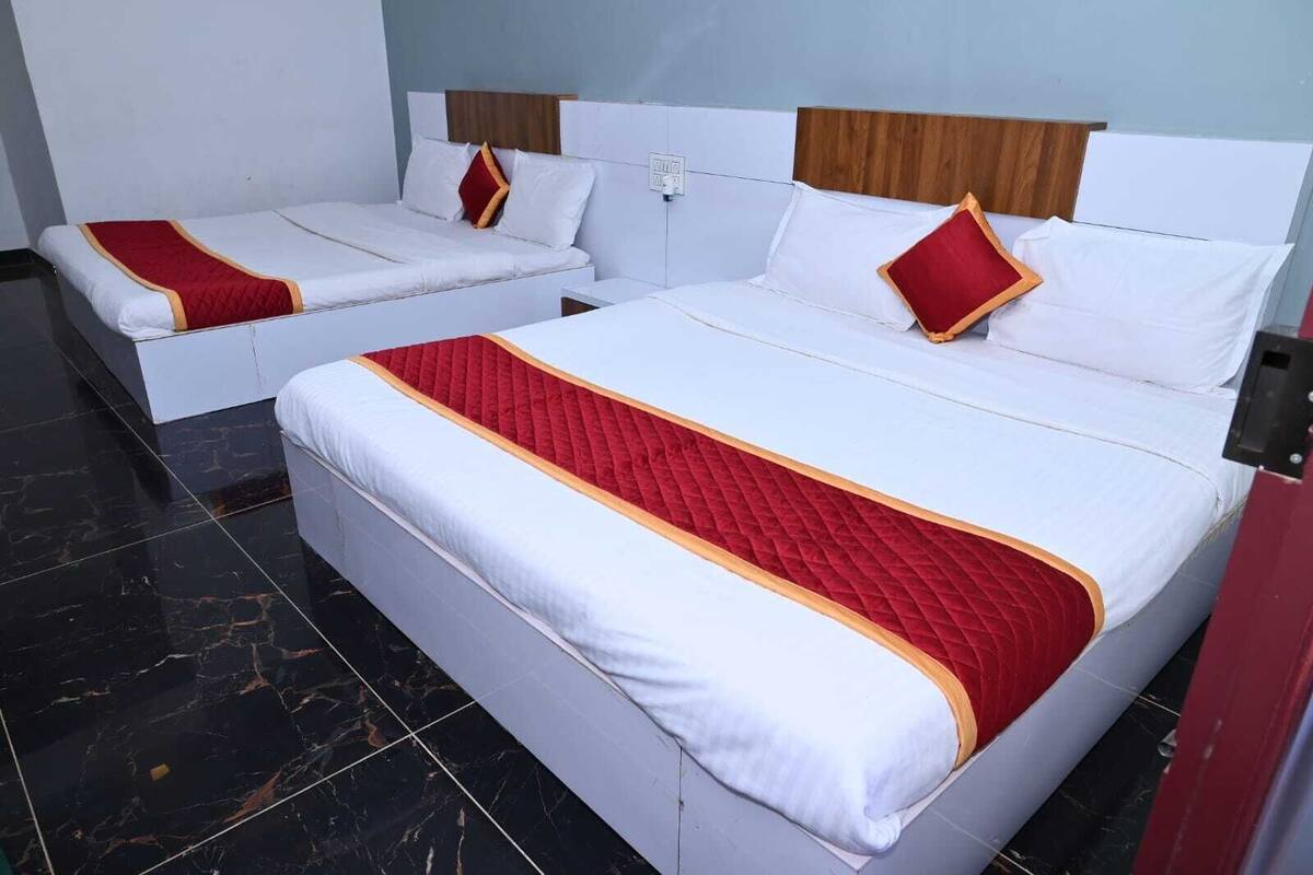 A hotel room with two beds, each with white bedding and red accents, and a marble-tiled floor.