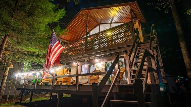 A wooden cabin with a balcony, an American flag, and string lights.