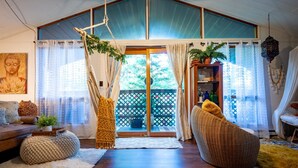 A spacious living room with a high ceiling, a large sliding glass door leading to a balcony, a sofa, a wicker chair, and a hanging plant.