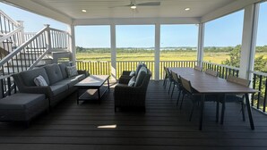 A covered outdoor deck with a sofa, chairs, and a table, overlooking a grassy landscape.