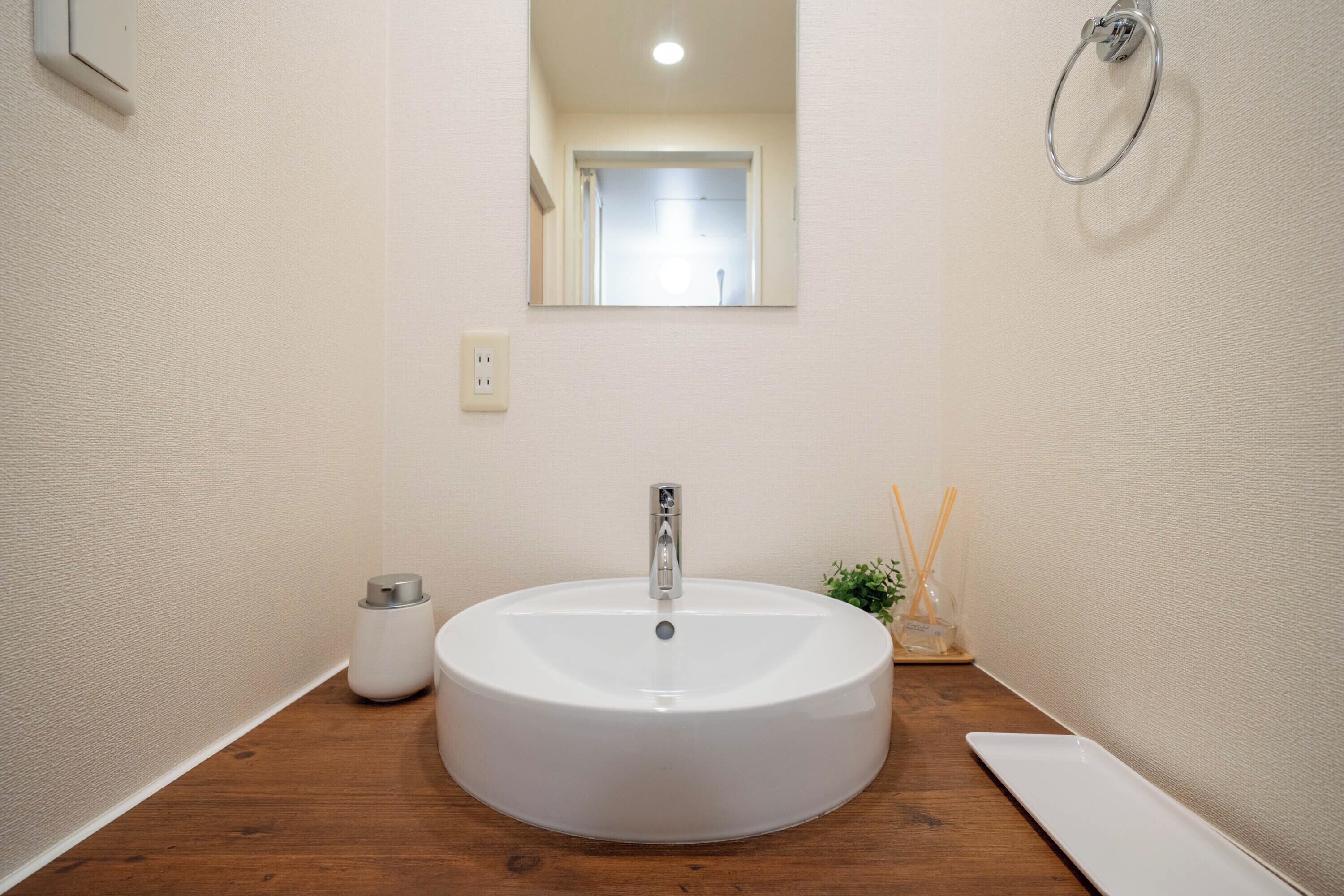 Ein Badezimmer mit einem runden weißen Waschbecken, einer Holzauslage, einem Spiegel und einer kleinen Pflanze.