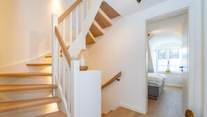 A modern staircase with wooden steps and white walls, leading to a bedroom with a bed and a window. - Haus Rosi - Holiday home in Westerland with sauna and garden. Pets are (Sylt)