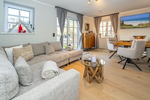 Un salon moderne avec un canapé gris, une table basse en verre et un coin repas comprenant une table et des chaises en bois.