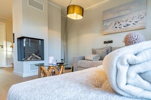 Un salon chaleureux avec une cheminée, un canapé, une table avec une bougie et un tableau accroché au mur.