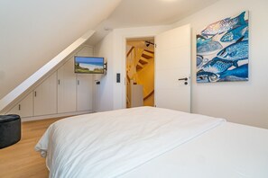 Une chambre à coucher avec un lit, un téléviseur fixé au mur et un tableau.