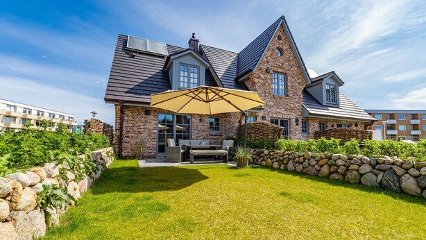 A large brick house with a stone wall and a patio area with a table and chairs. - Haus Rosi - Holiday home in Westerland with sauna and garden. Pets are (Sylt)